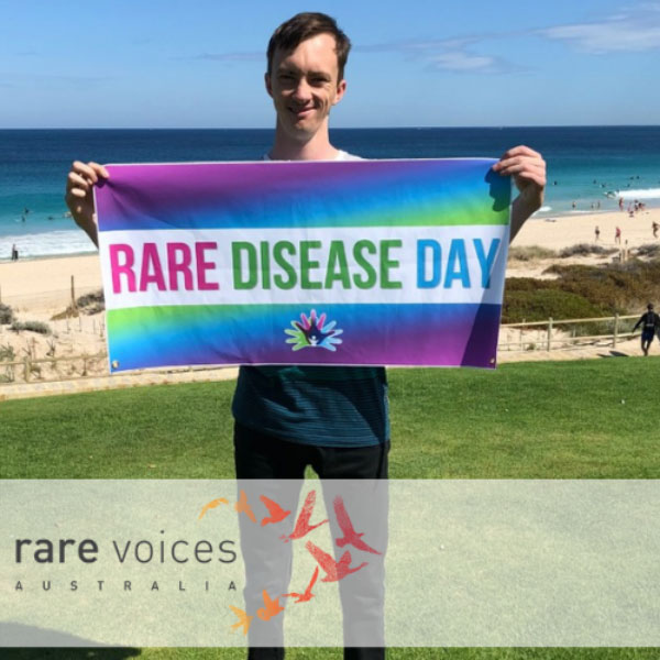 Story-Andrew Photo of Andrew holding the Rare Disease Day banner.