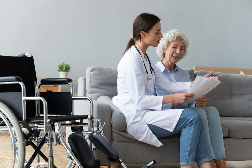 Woman sitting on a couch speaking with a health professional. A wheelchair is near the couch