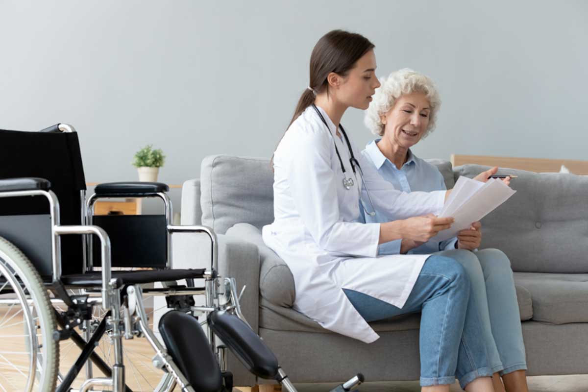 Health professional speaking with woman sitting on a couch with a wheelchair to the side